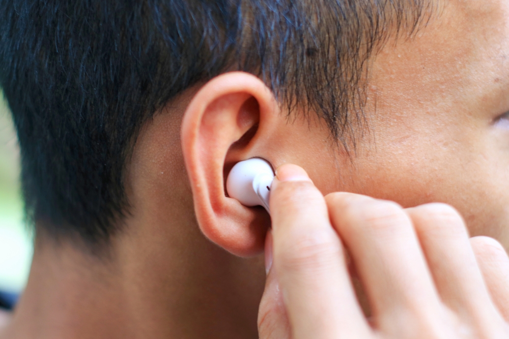 A person inserting a white wireless earbud into their ear, shown in close-up from the side.